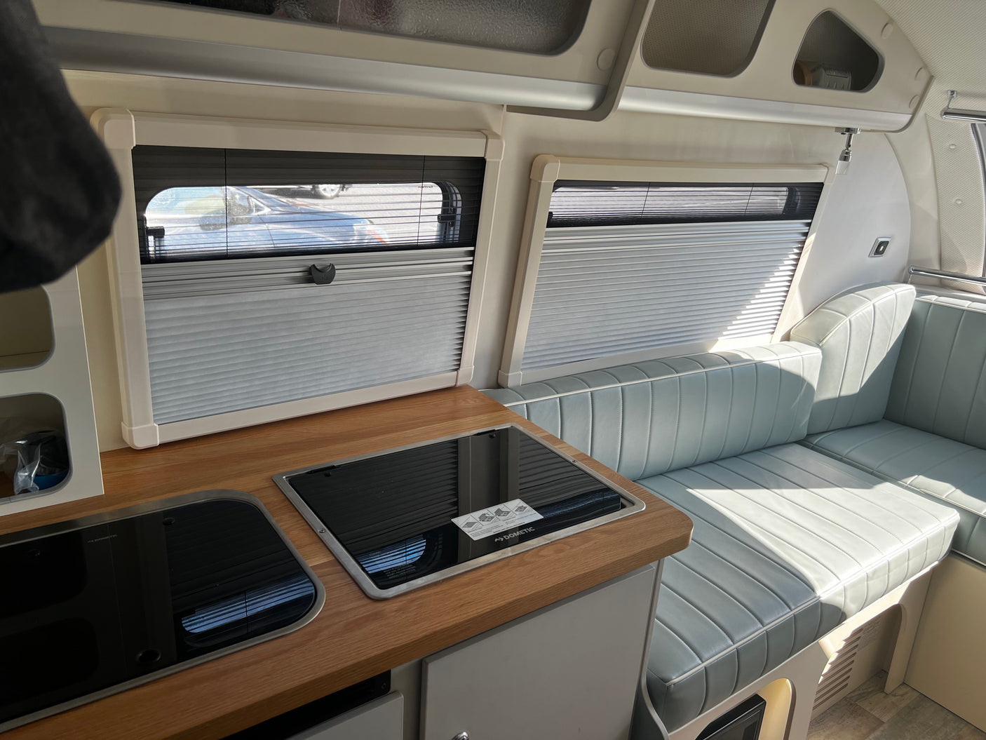 Spacious RV rental interior featuring a modern kitchenette with Dometic appliances, cozy bench seating, and pleated window blinds.