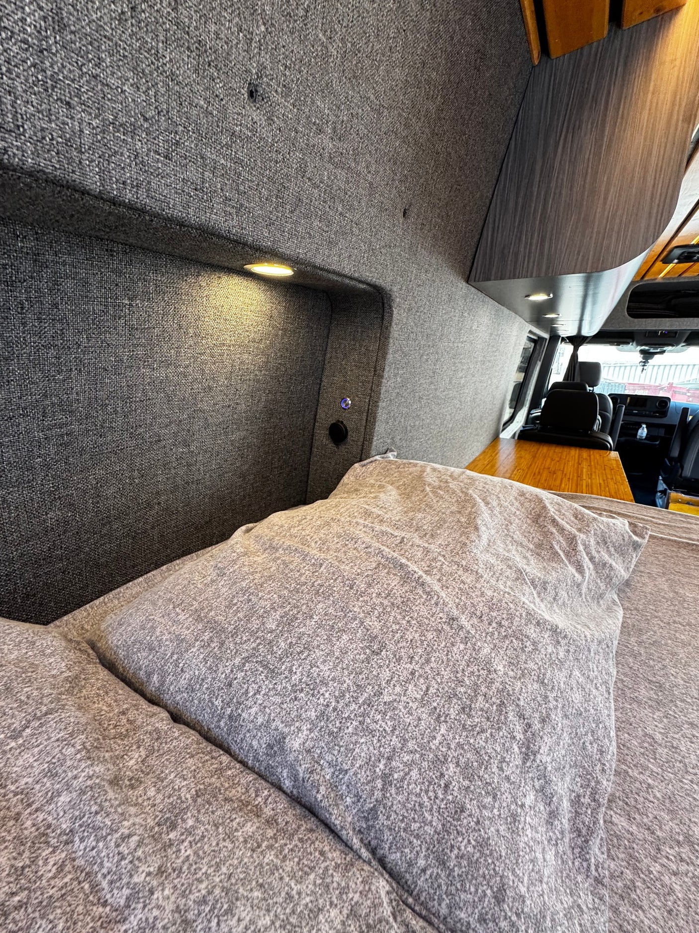 Cozy RV rental interior. Fabric walls, warm lighting, comfortable bed & view to the cockpit. Perfect for road trips!