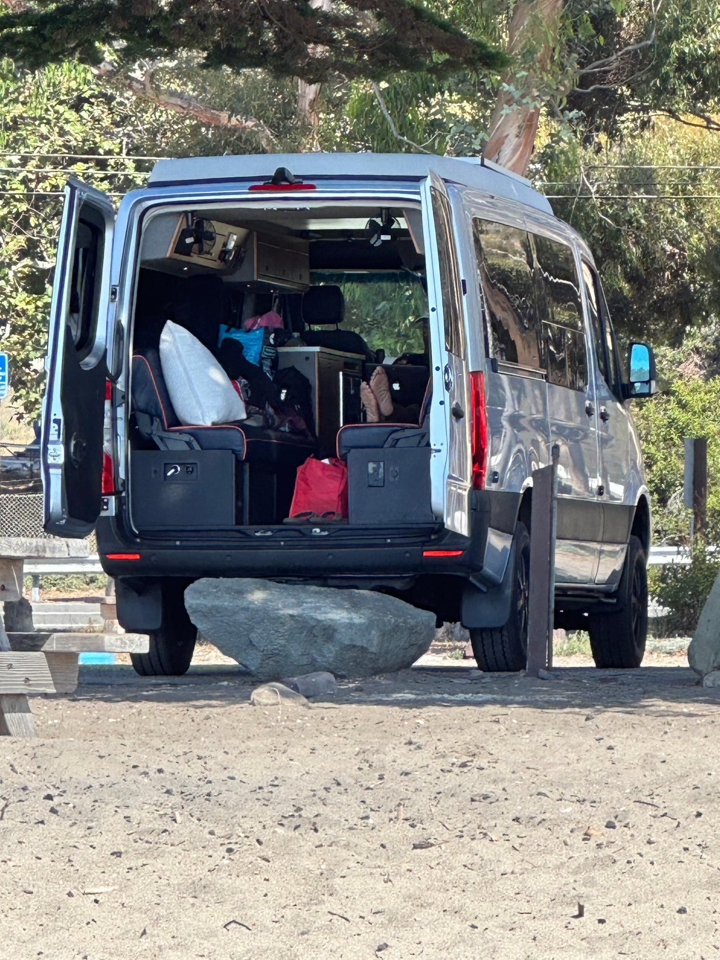 Rear view of a silver RV rental camper van, doors open, revealing a comfortable interior ideal for travel.