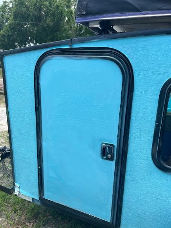 This bright blue teardrop RV rental features a sturdy door & textured exterior, perfect for adventure.