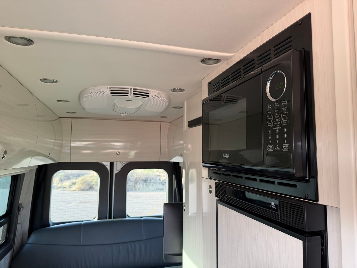 RV rental interior features Dometic AC, High Pointe microwave, and Norcold refrigerator amidst overhead cabinets and rear seating.