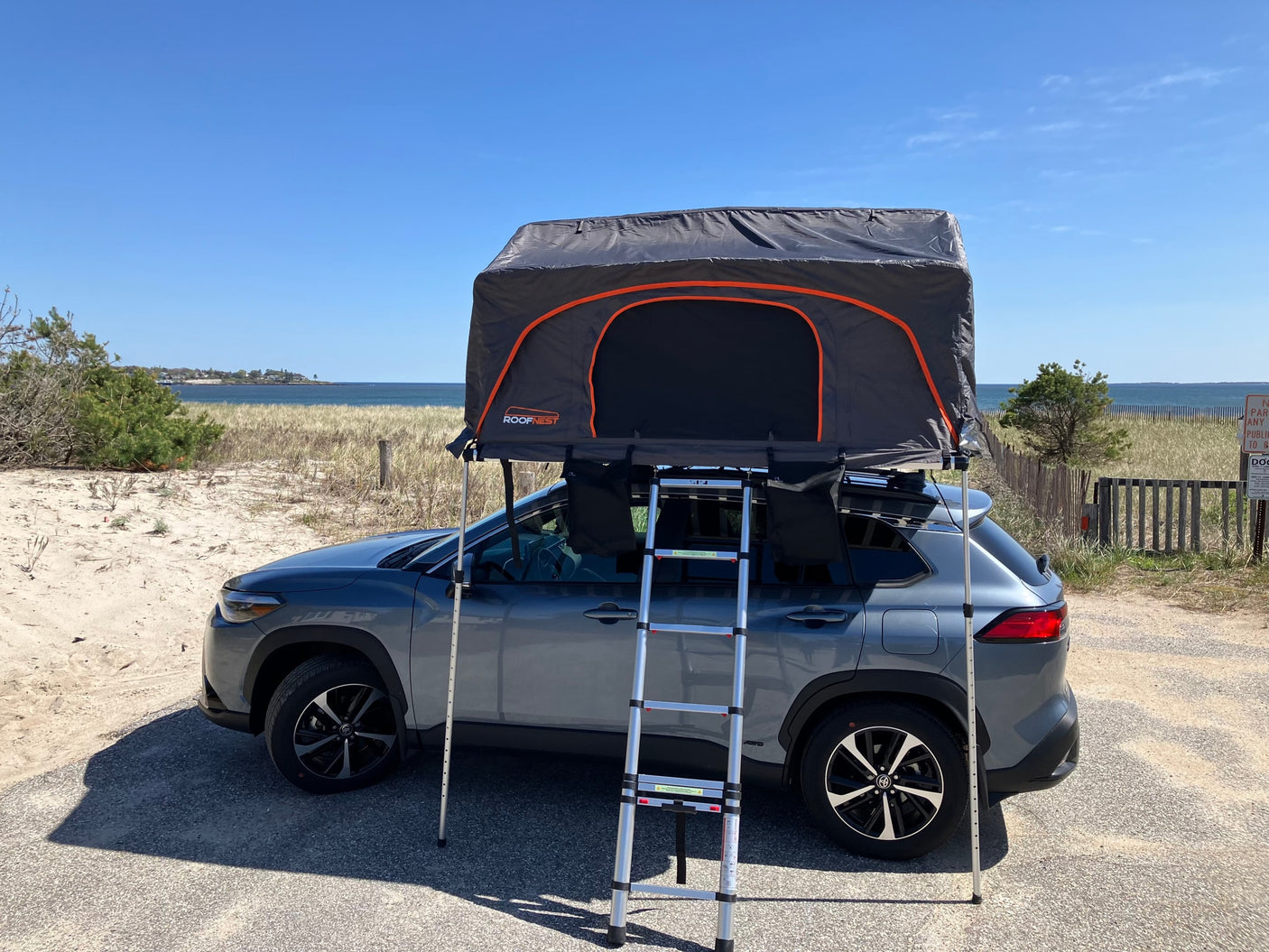 Grey SUV with a deployed Roofnest rooftop tent on a sandy beach. A compact RV rental alternative for camping adventures.