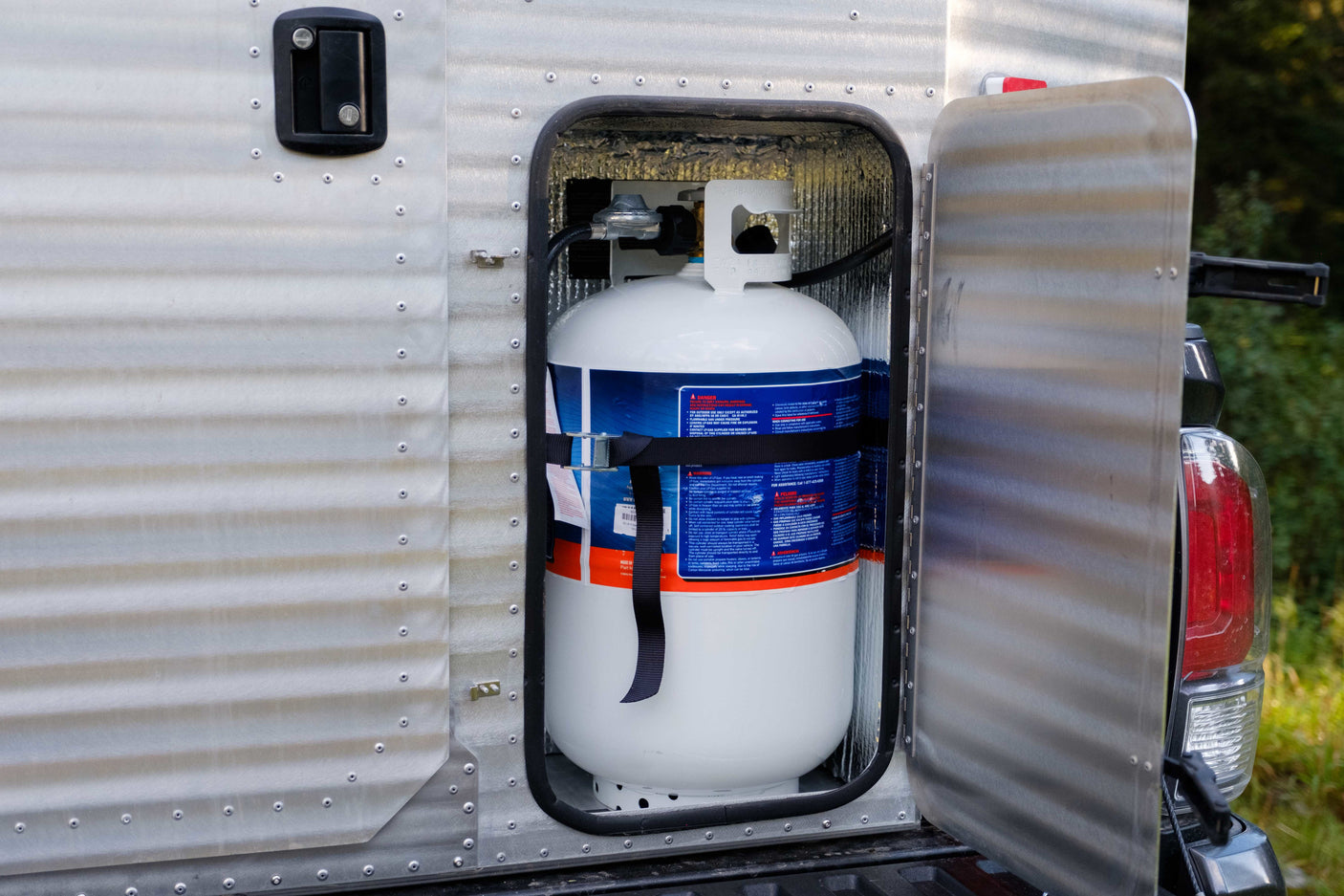 A white propane tank is securely stored in a side compartment of an RV rental, essential for camping adventures.