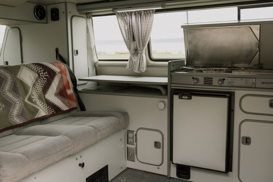 Explore a cozy RV rental interior with a compact kitchen, comfortable bed, and versatile table, ready for your next adventure.