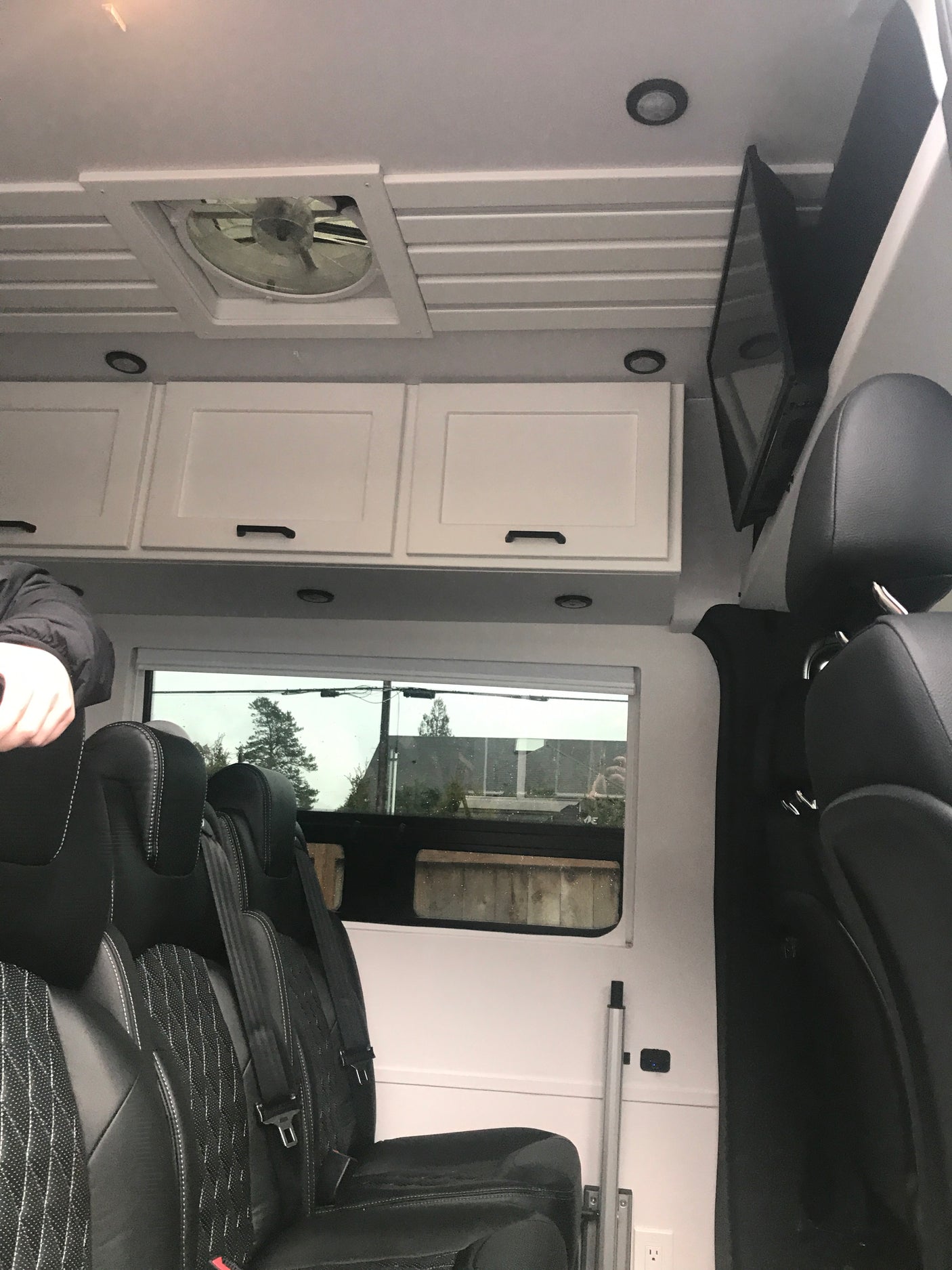 Spacious RV rental interior with black leather seats, overhead storage, ceiling fan, and mounted TV. Ready for your road trip!