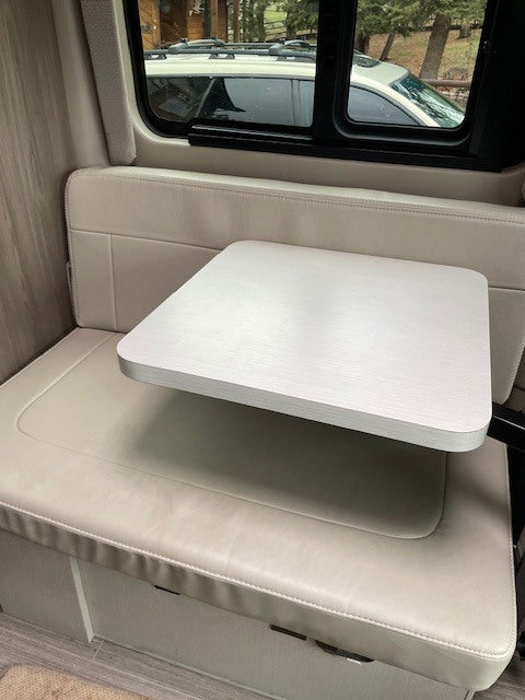 Bright RV rental interior showing a small dining table and bench seating by a window with an outdoor view.