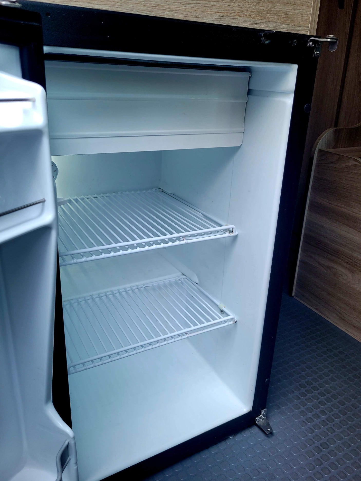 Clean, empty RV rental fridge interior with wire shelves and a small top freezer, ready for your trip's provisions.