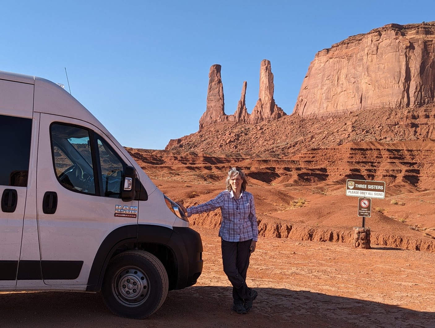 RV rental adventure: woman and van at Monument Valley's Three Sisters formations. Iconic desert landscape.