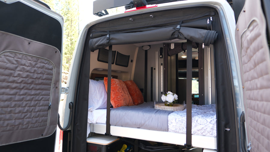 Cozy RV rental bed in a camper van with open rear doors revealing nature. Perfect for van life travel.