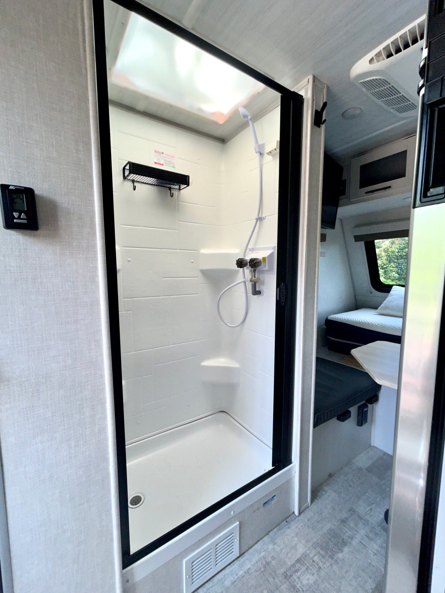 RV rental: Bright shower with digital thermostat, clear door, and a cozy sleeping area visible beyond.