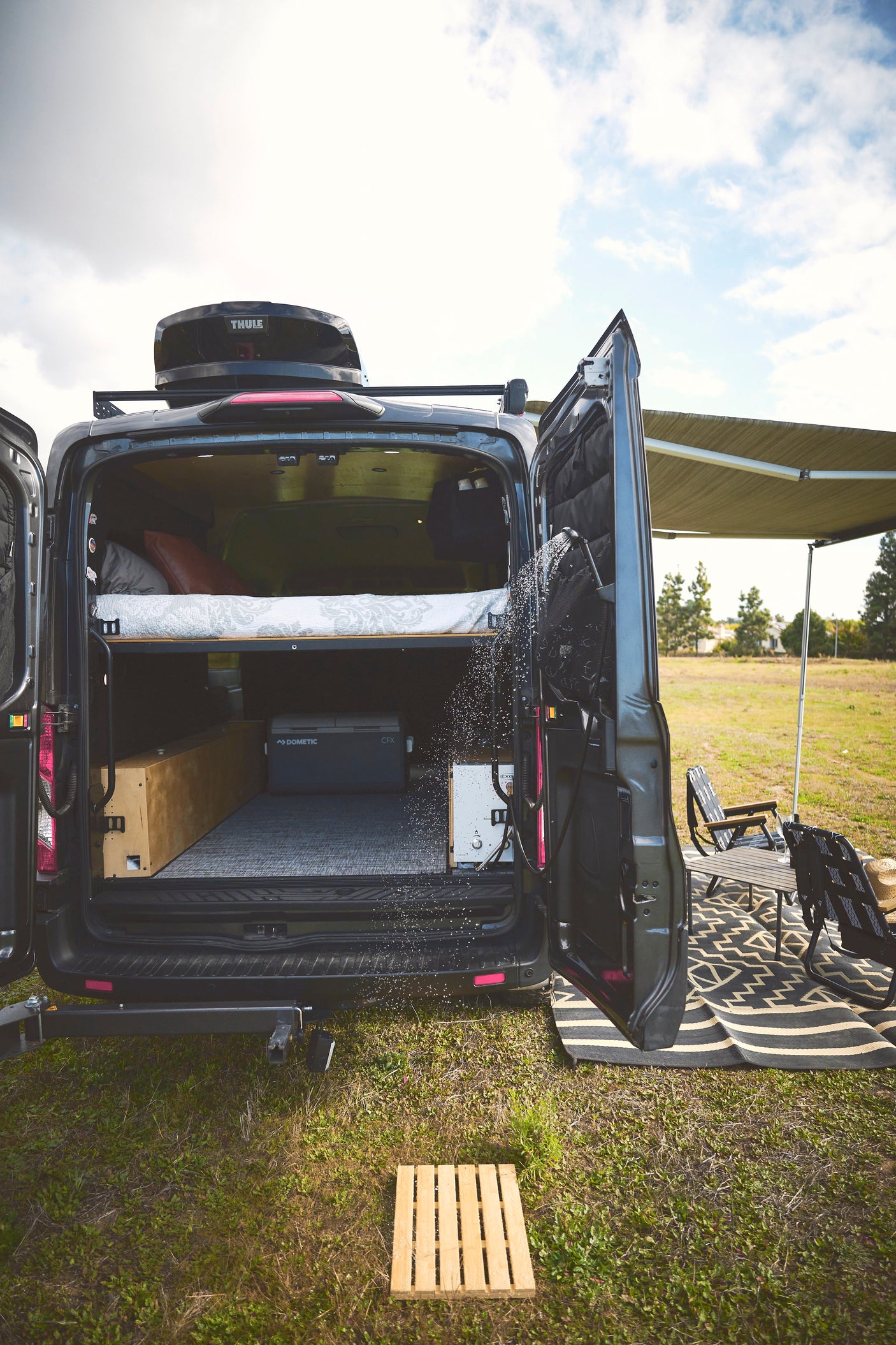 Experience comfort with this rv rental! A camper van with an outdoor shower, cozy bed, and shaded outdoor seating area for camping.