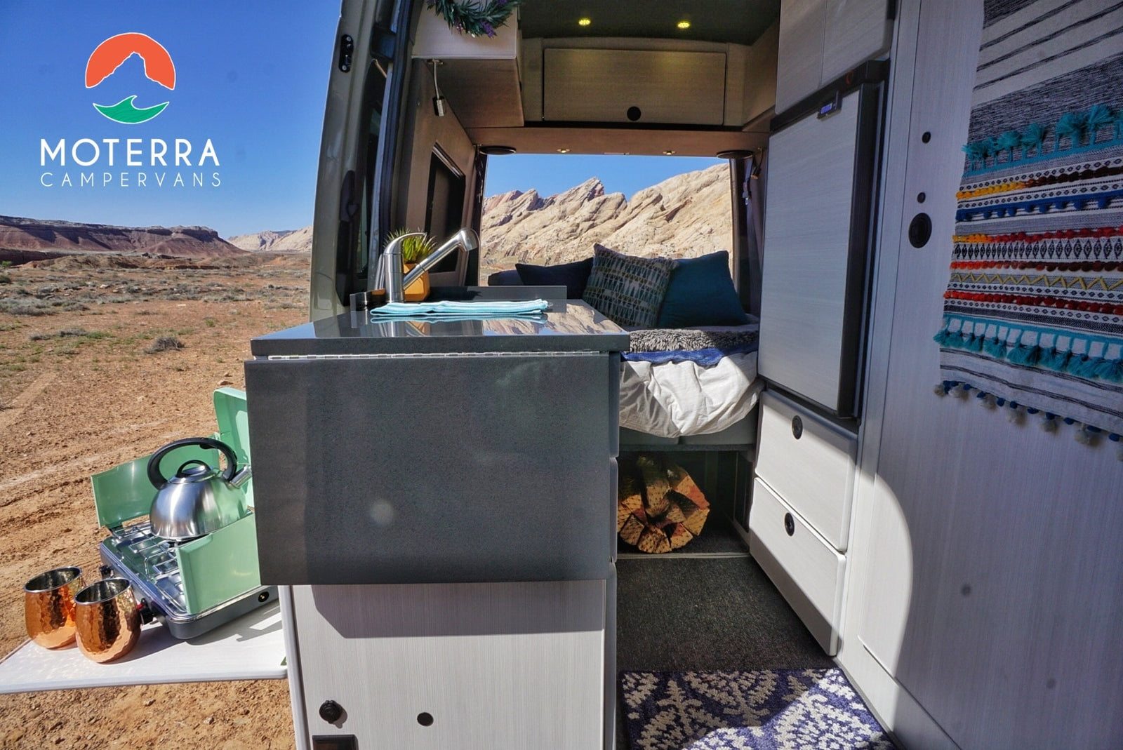RV rental adventure! Modern campervan interior with kitchen, cozy bed, outdoor cooking setup, & stunning desert views.