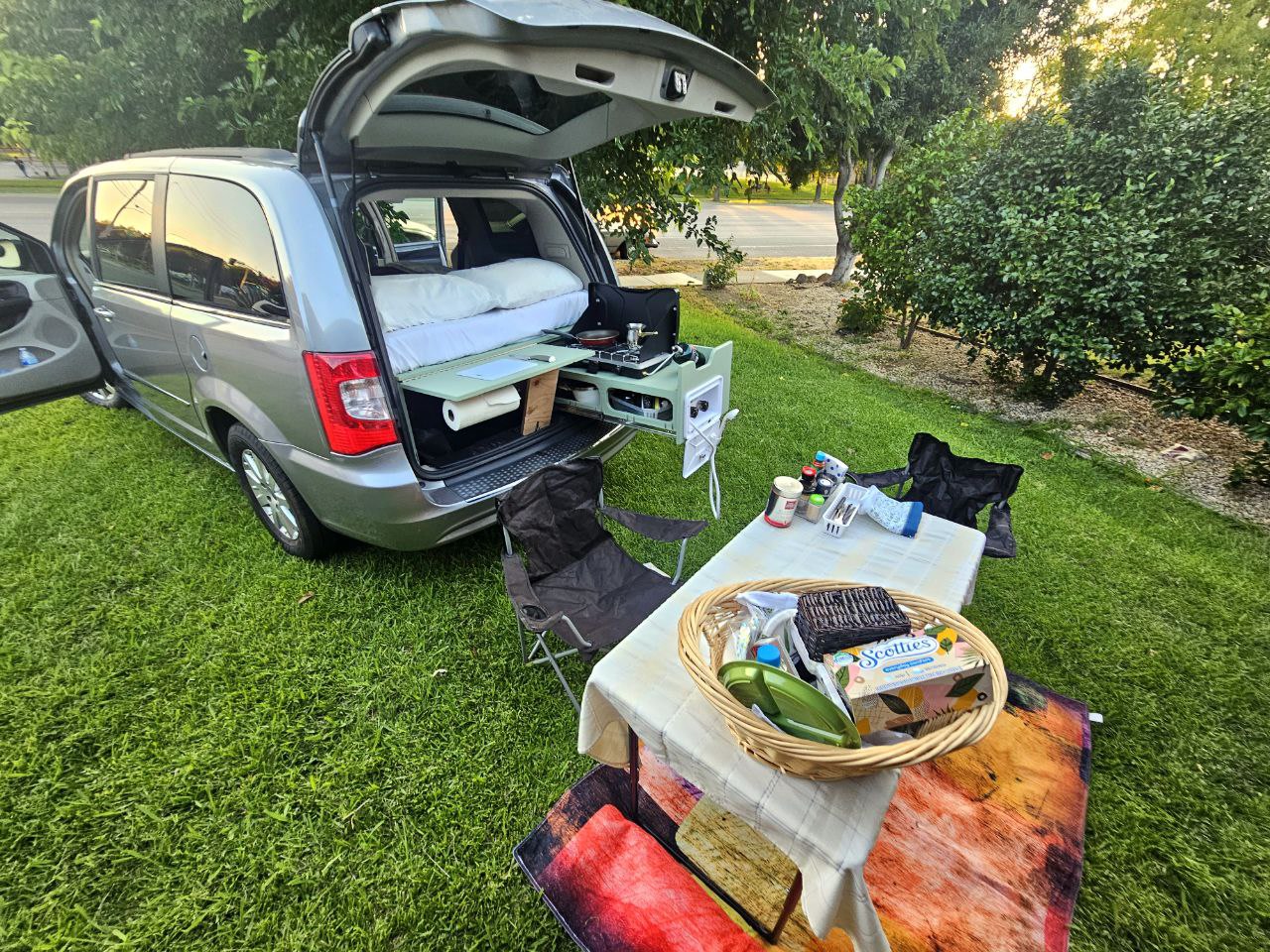 This RV rental shows a minivan converted for camping with a bed, pull-out kitchen, and an outdoor dining setup.