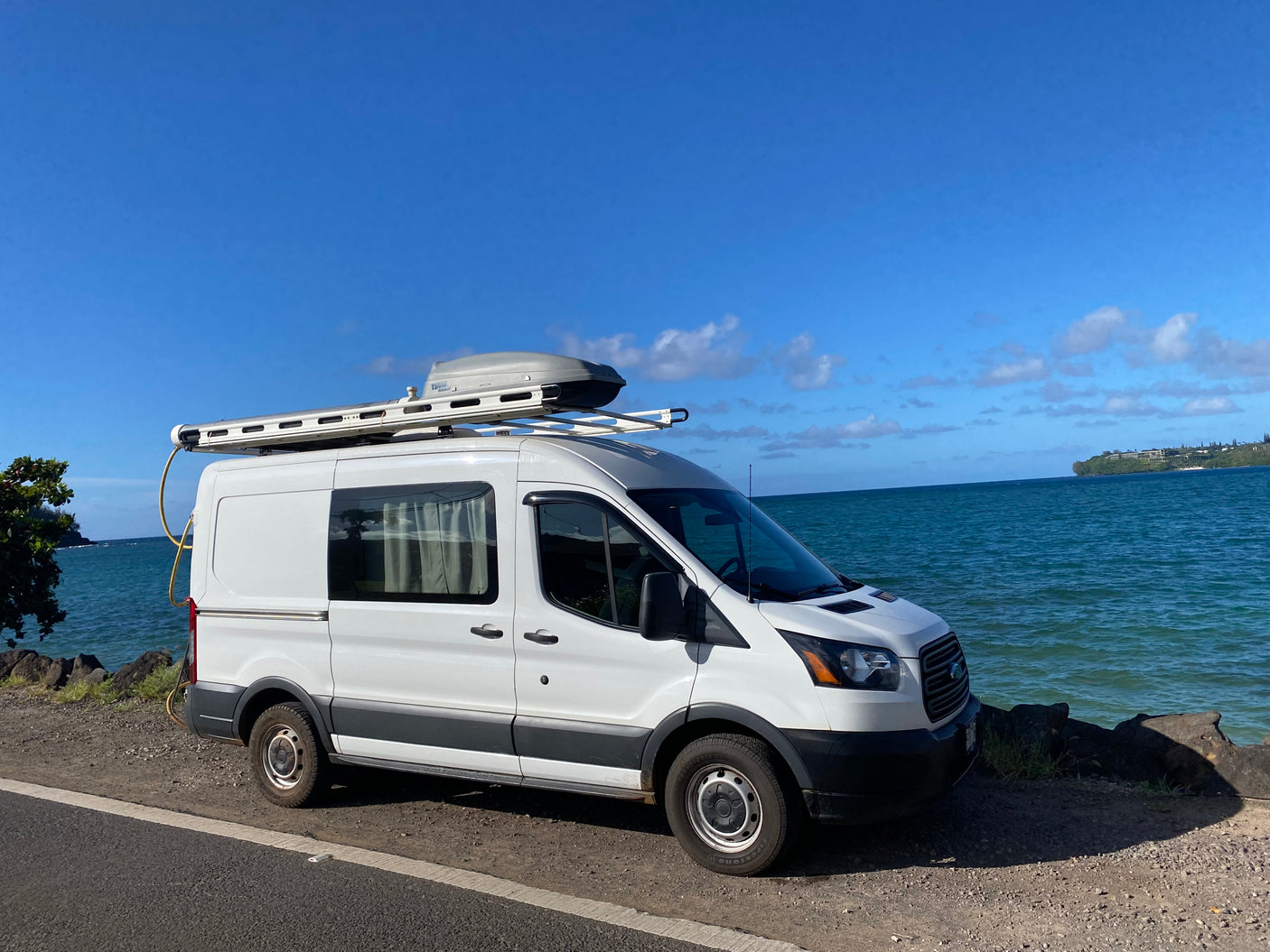 White campervan RV rental parked beside a tranquil blue ocean under a clear sky. Ideal for road trip getaways.