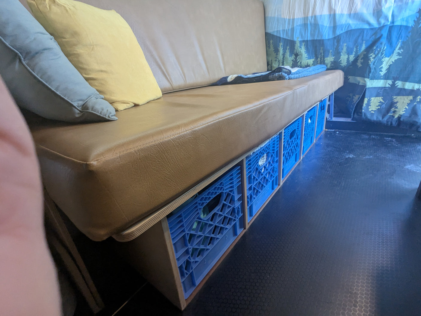 Practical RV rental interior: brown bench with pillows, custom storage featuring blue milk crates & wood framing.