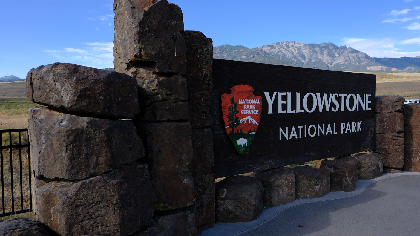 Yellowstone National Park entrance sign, framed by stone pillars, mountains visible. Ideal for an RV rental trip!