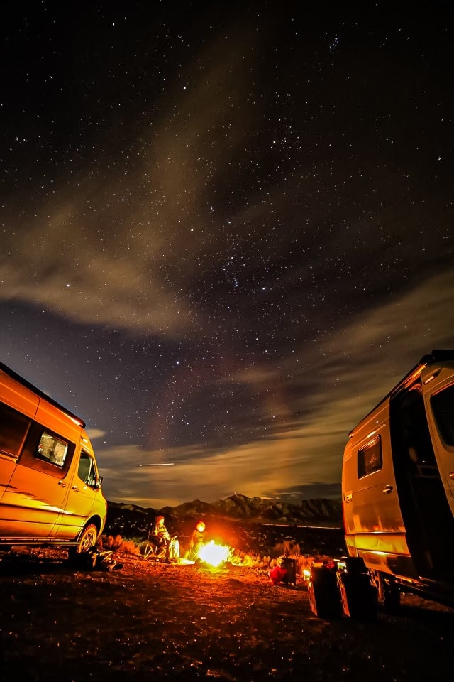 RV rental adventure: Two camper vans, people by a campfire, & a stunning starry night sky over mountains. — photo 4