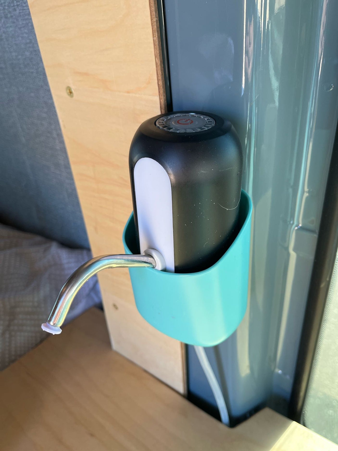 Black & white automatic water dispenser in a teal holder, mounted in an rv rental, offering easy water access.