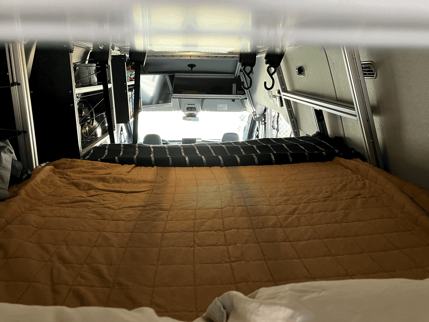Inside an rv rental: the comfortable bed of a customized camper van, looking to the front cabin.