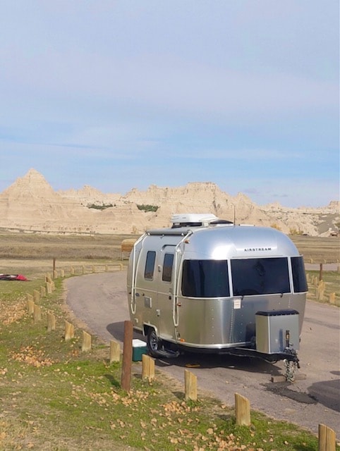 This sleek Airstream rv rental sits on a campsite road, framed by the distinctive Badlands geology under a clear sky.