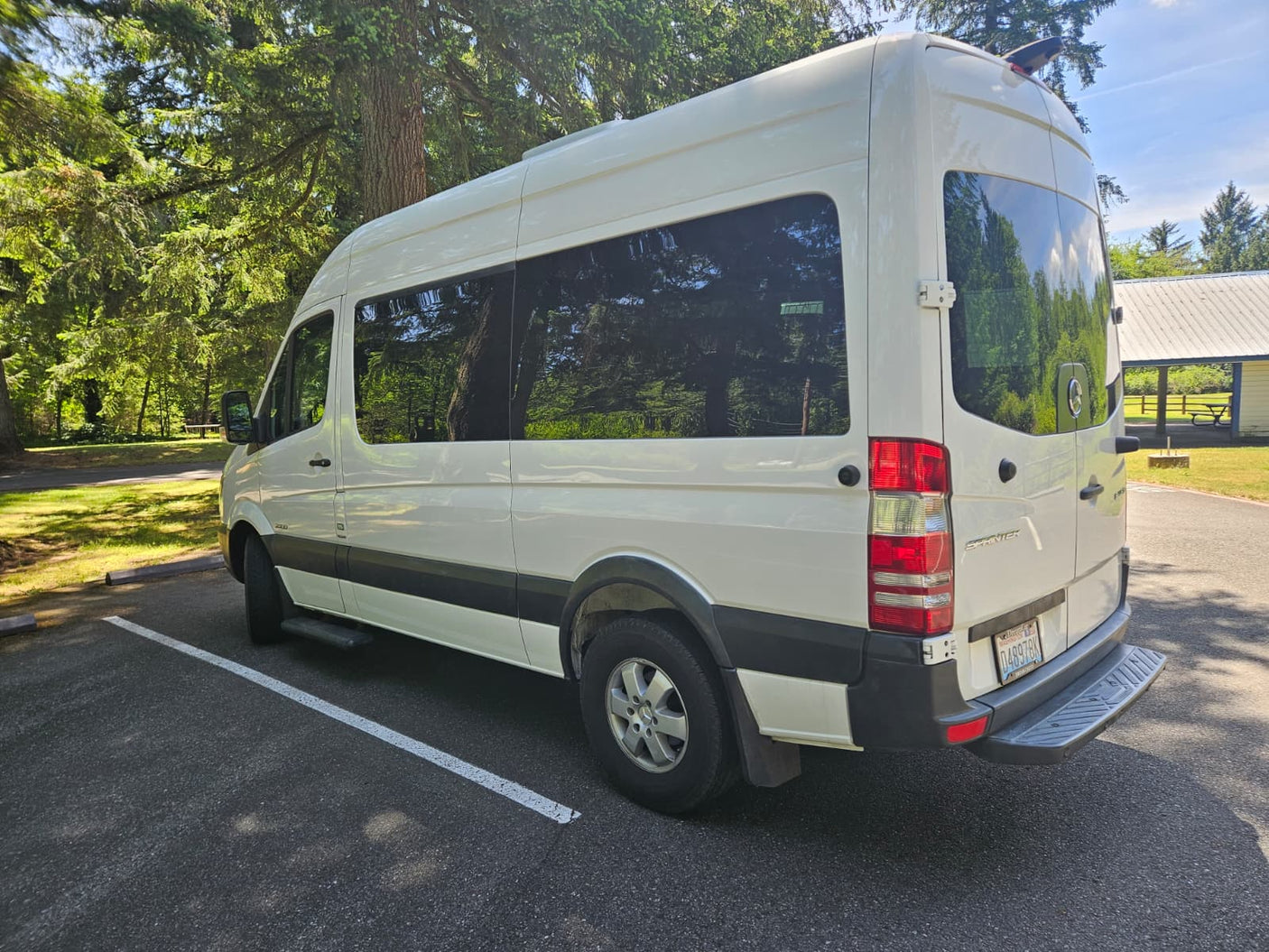 This white Mercedes Sprinter van RV rental is parked in a sunny, tree-lined park, perfect for your next camping trip.
