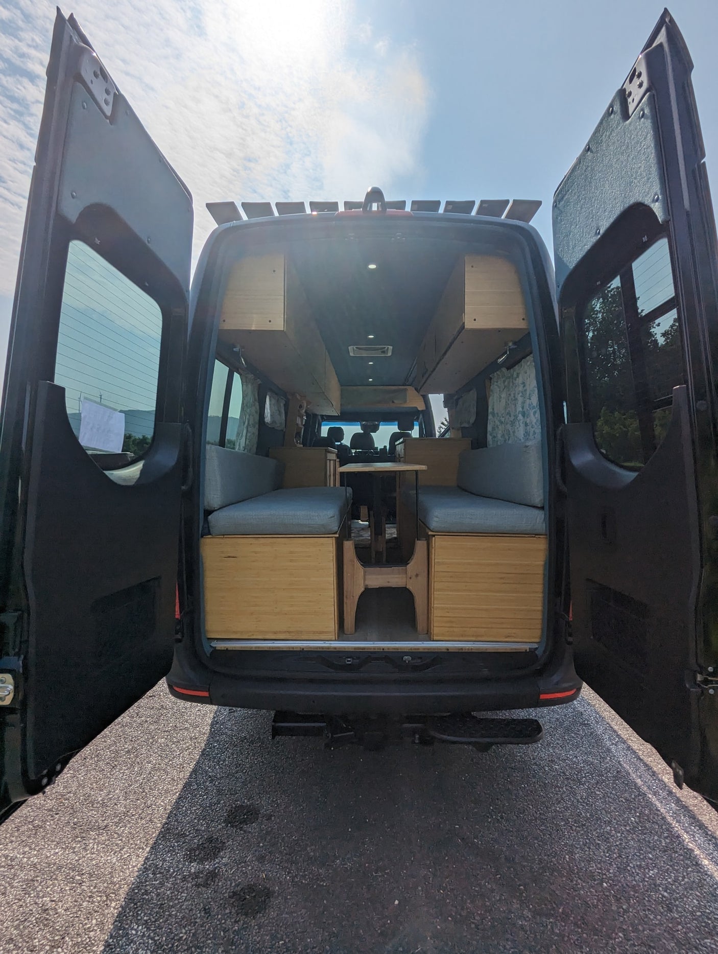 with a large arched bridge. Ready for your next adventure.|Black Mercedes-Benz Sprinter RV rental parked by a river with a scenic bridge under a blue sky.|Cozy rv rental interior with light wood cabinetry