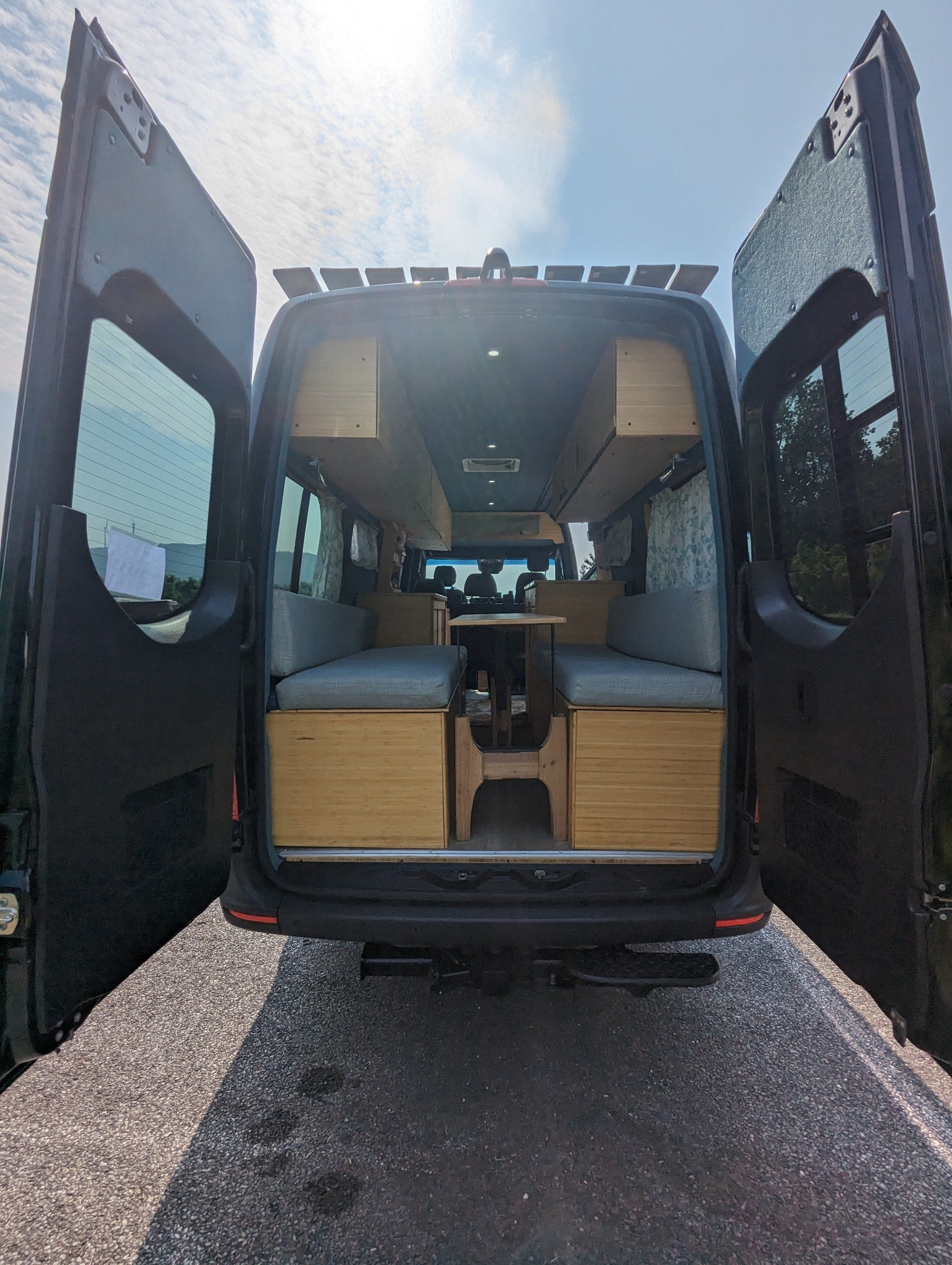 with a large arched bridge. Ready for your next adventure.|Black Mercedes-Benz Sprinter RV rental parked by a river with a scenic bridge under a blue sky.|Cozy rv rental interior with light wood cabinetry