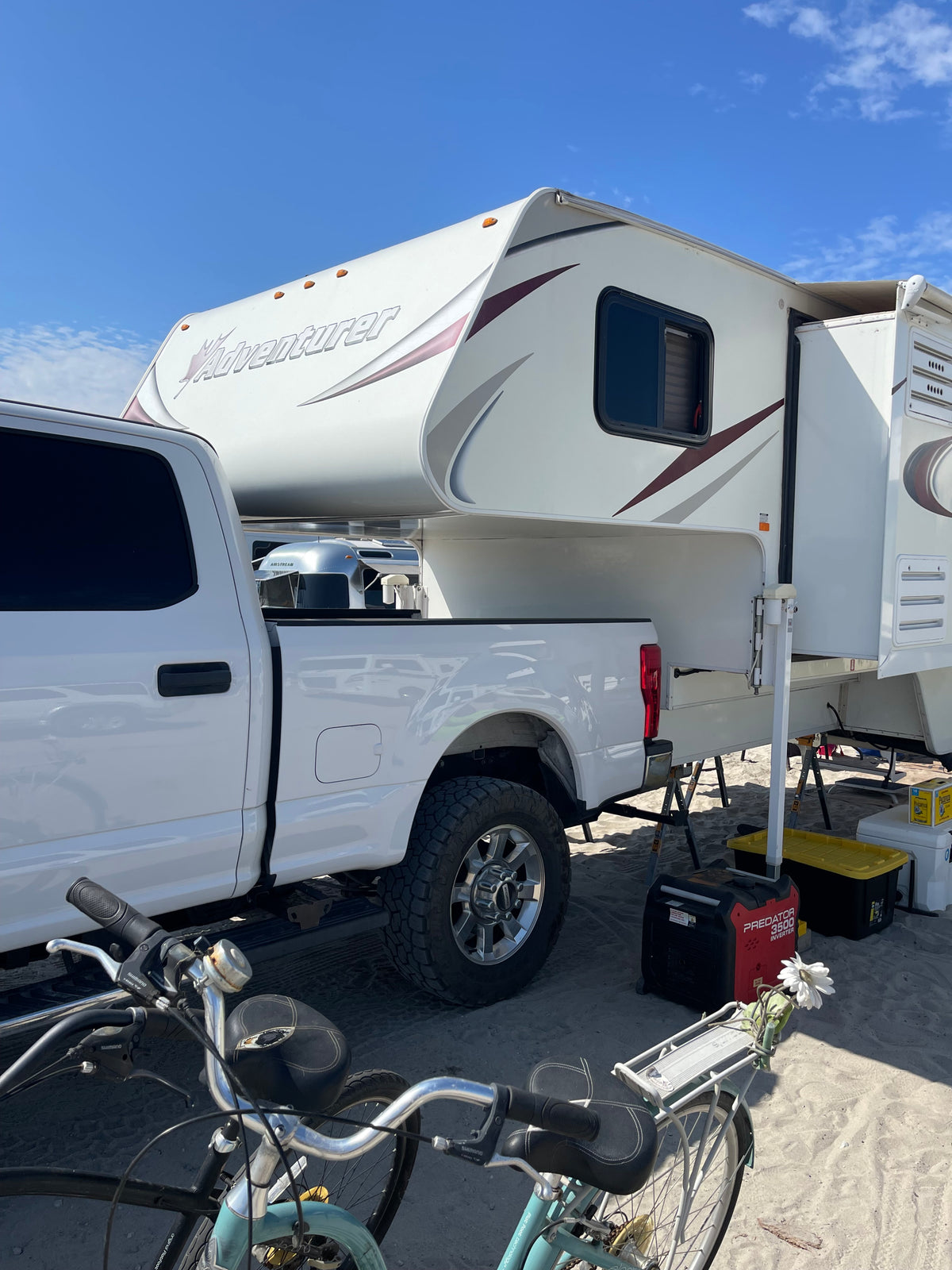 Adventurer truck camper on a Ford pickup, set up on sand with bikes and a generator. Perfect for an RV rental adventure! — photo 9