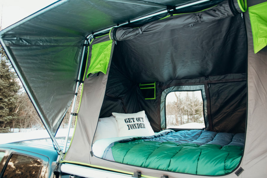 Inside a comfy rooftop tent from an RV rental, ideal for winter camping in nature with a cozy bed.