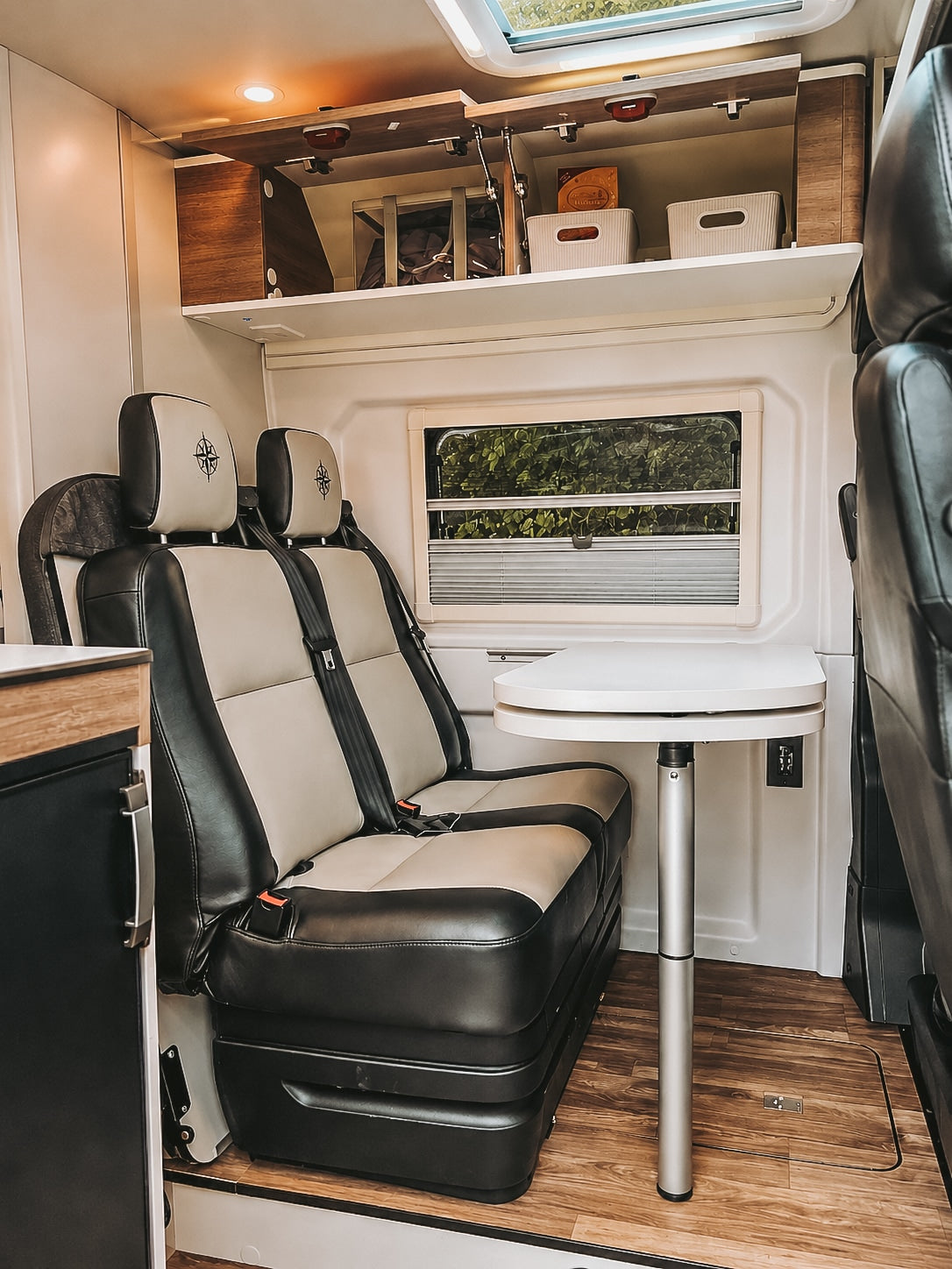 Cozy RV rental interior with comfortable two-tone seats, adjustable dining table, and overhead storage for organized travel.