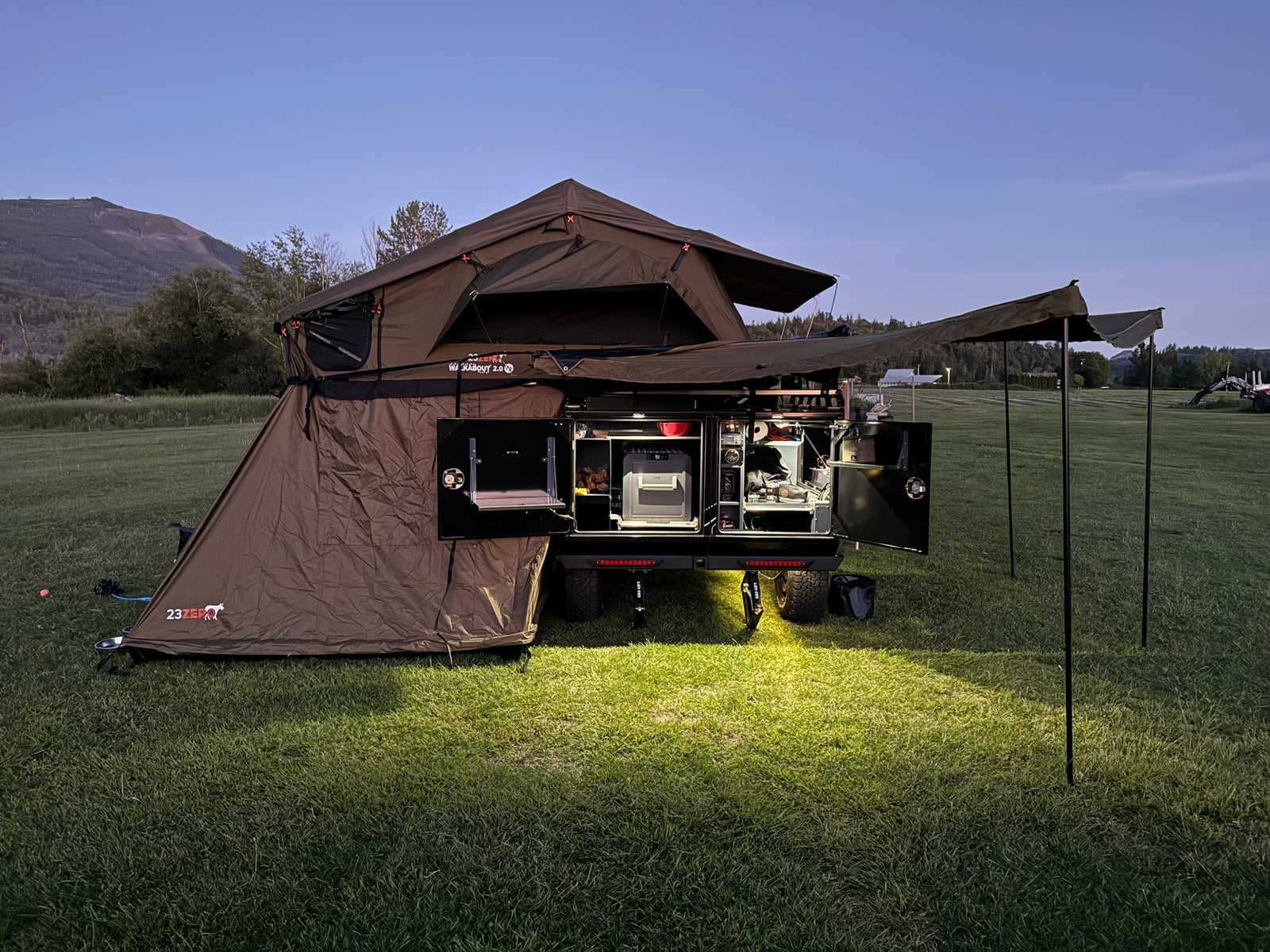 Modern overland camper trailer with rooftop tent and outdoor kitchen, perfect for an RV rental adventure at dusk.