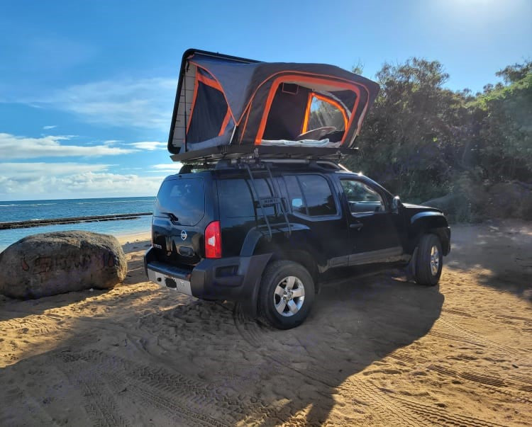 Black Nissan Xterra with rooftop tent on a sandy beach. Perfect RV rental for oceanfront overlanding adventures.