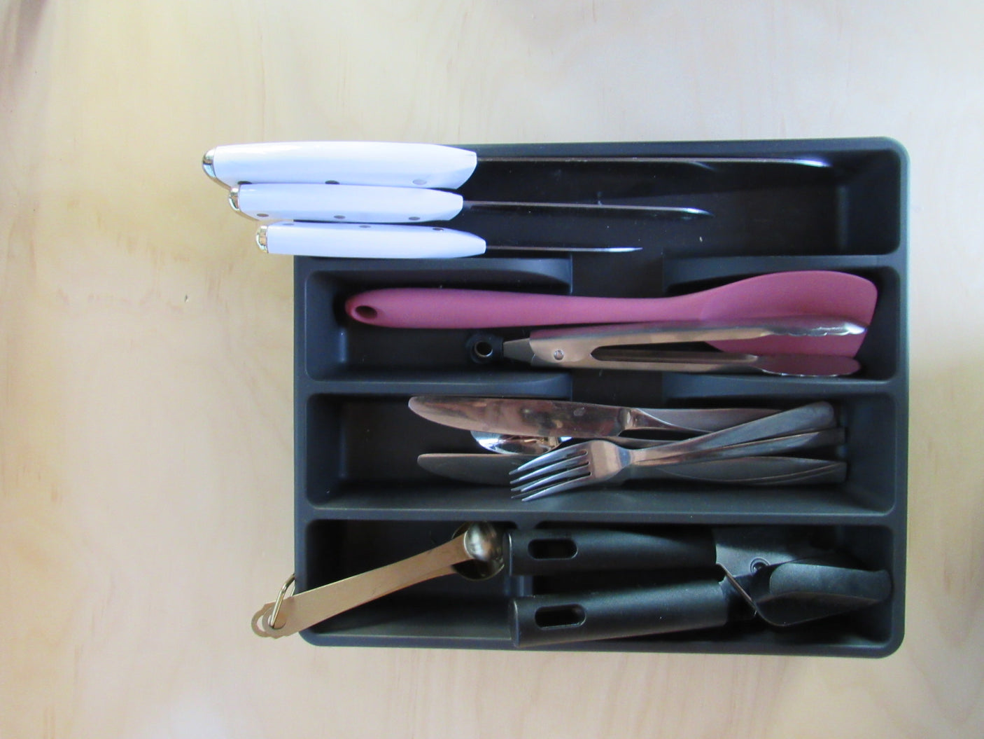 RV rental kitchen drawer organizer: white-handled knives, pink spatula, cutlery, and measuring spoons for tidy storage.