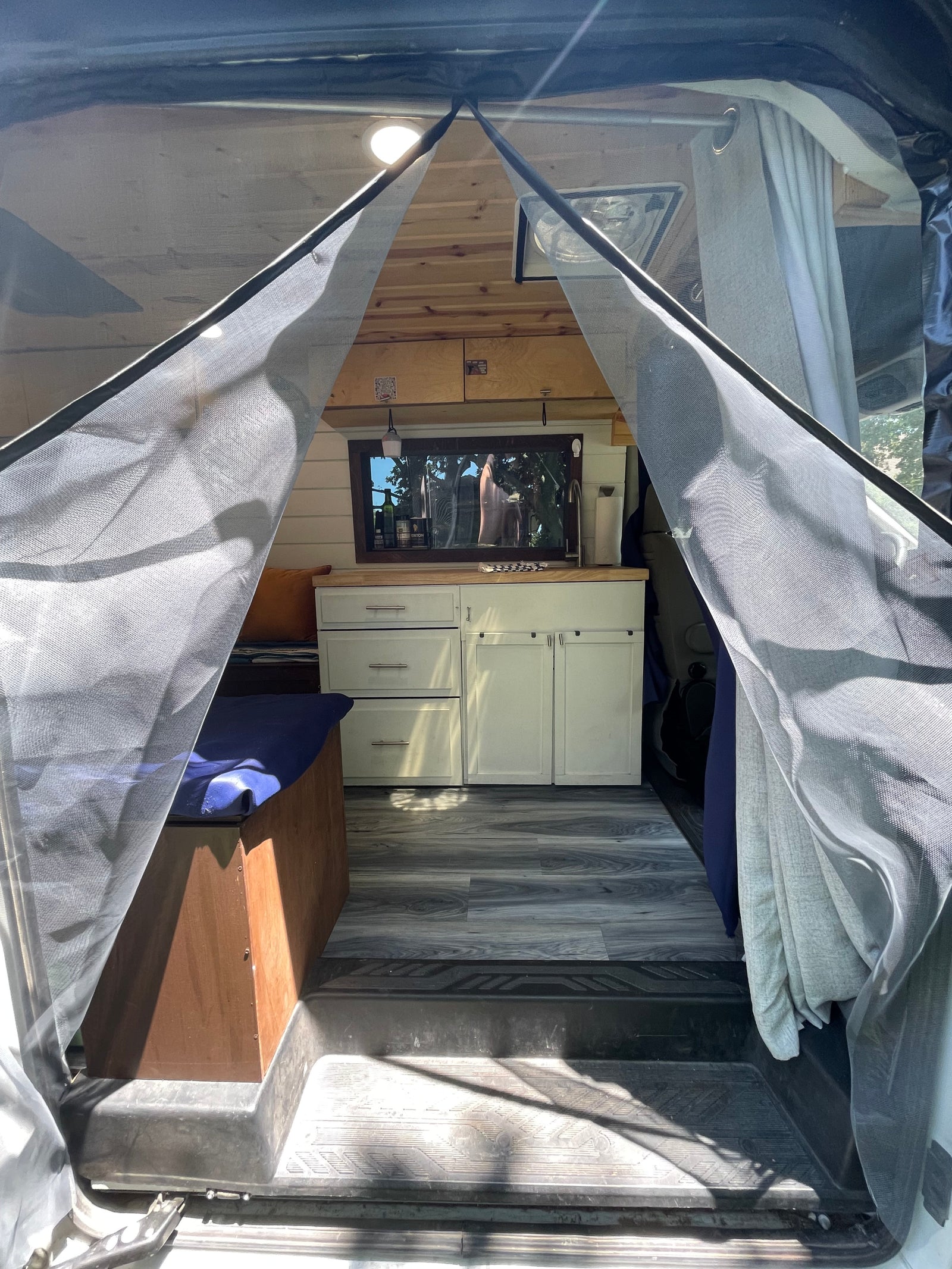RV rental interior: A cozy camper van with a kitchenette, bench, wood ceiling, and bug screen at the entrance.
