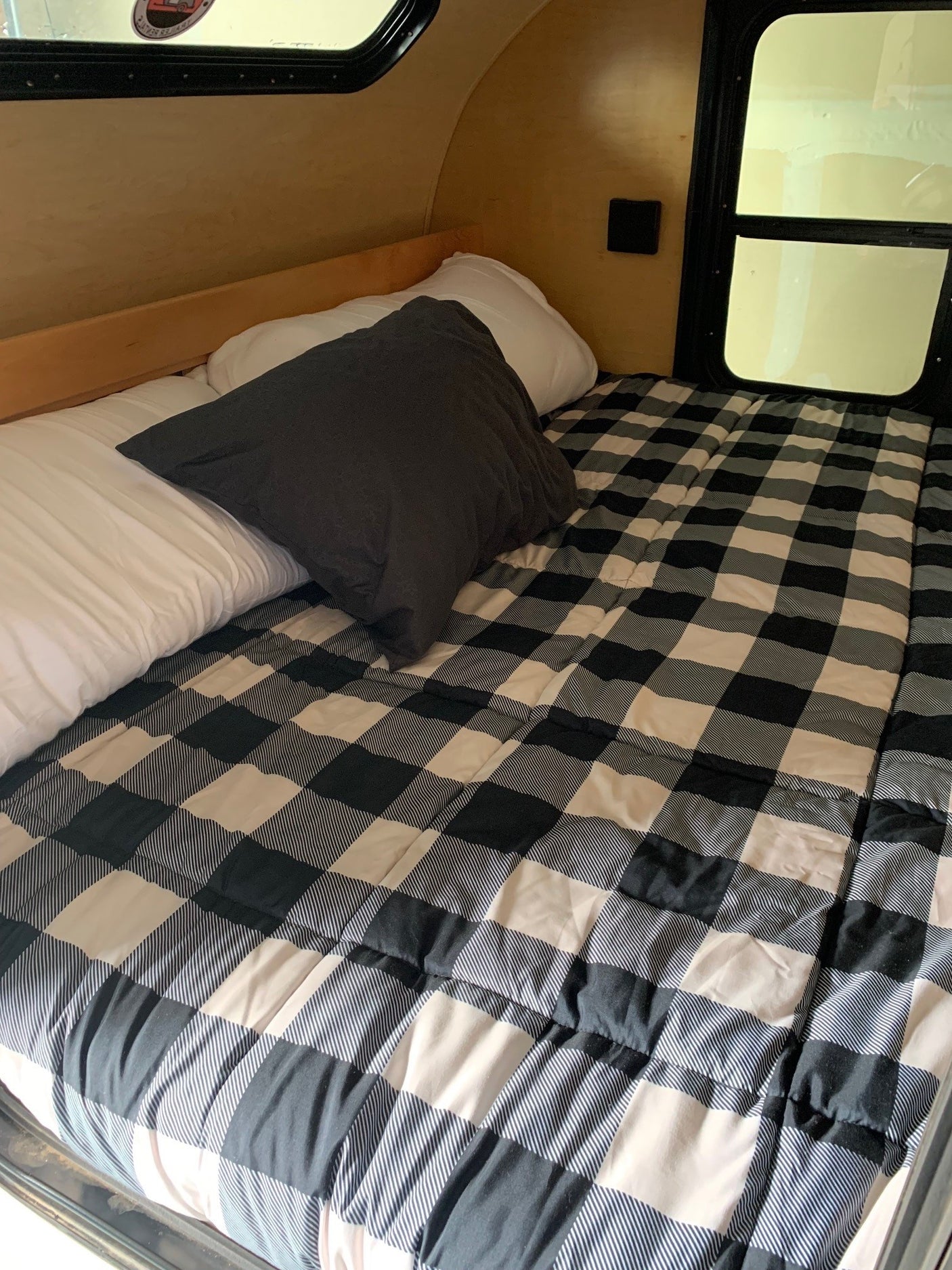 Cozy RV rental interior: a comfortable bed with white and dark pillows, covered by a black and white buffalo plaid comforter.