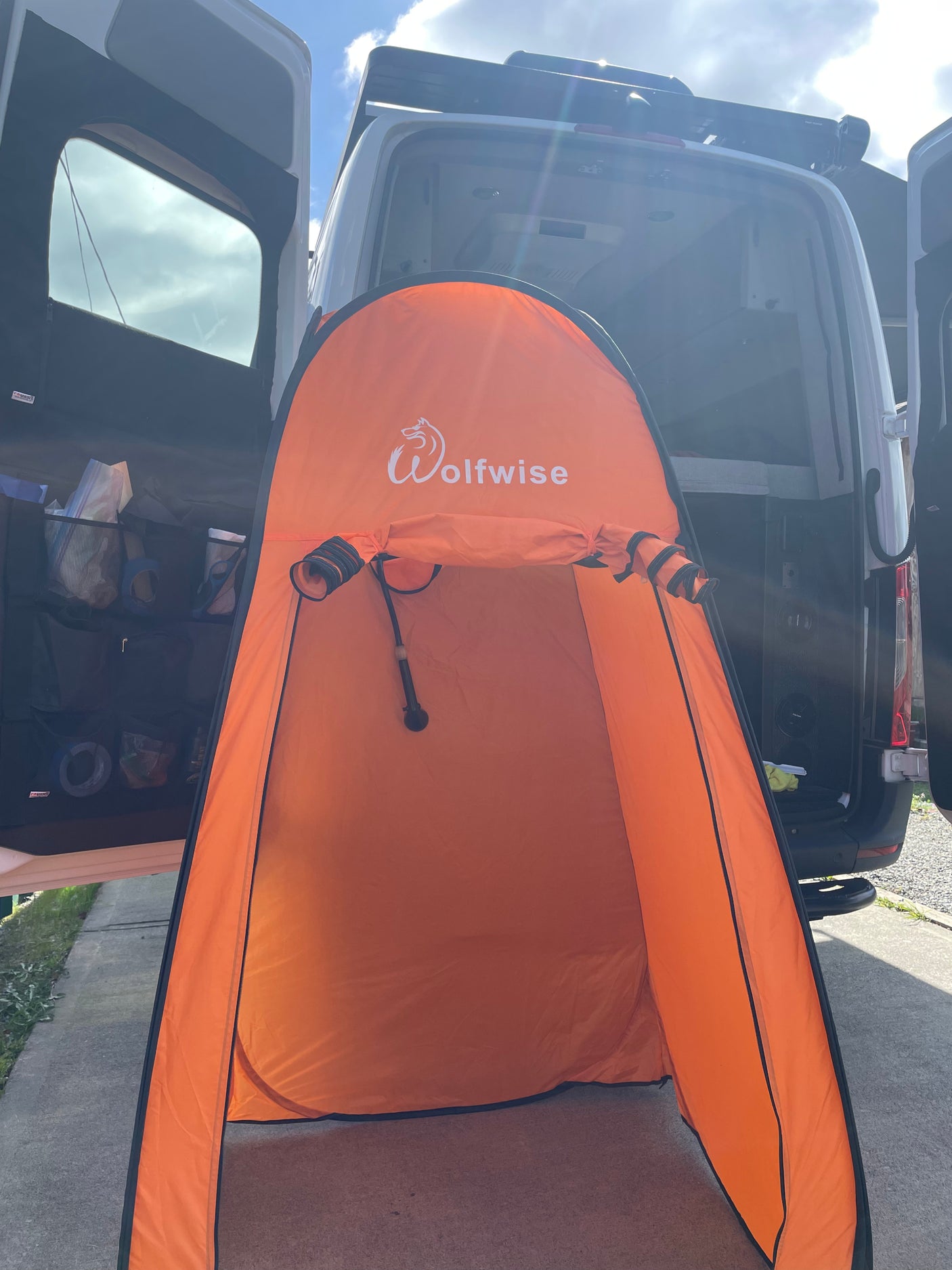 Orange Wolfwise pop-up privacy tent with shower inside, set up behind an RV rental van for convenient camping.
