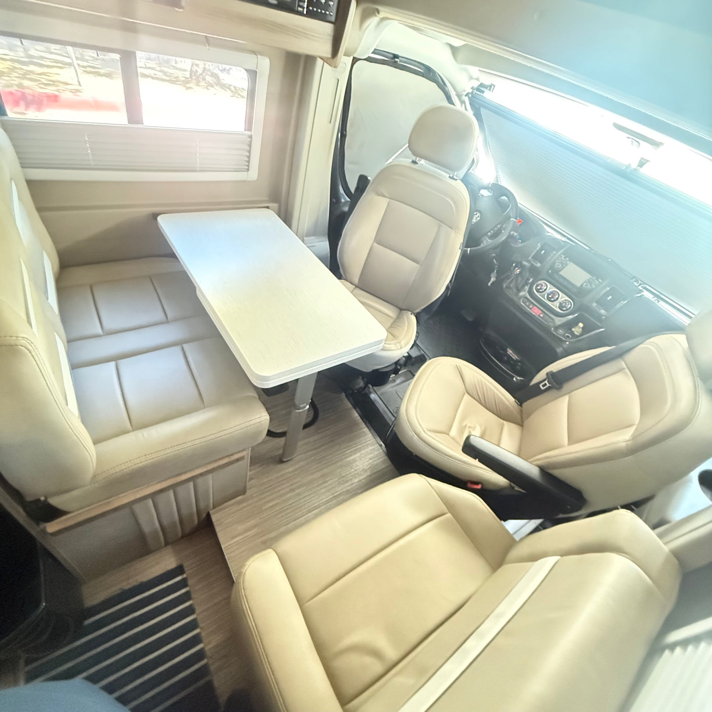 Interior of an RV rental showing cream seating, a central table, and the driver's area with dashboard. A comfortable travel space.