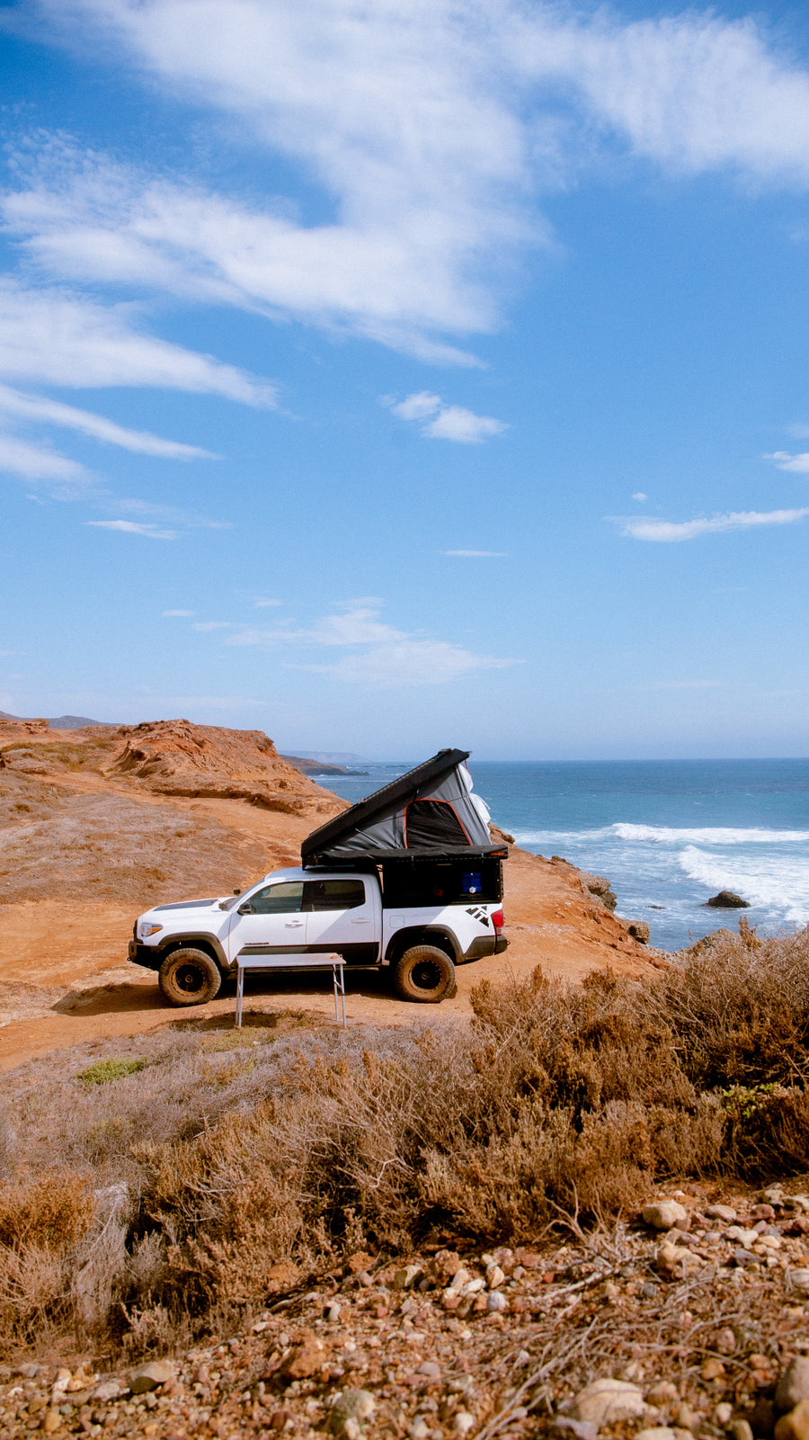 Coastal camping: White pickup truck with deployed pop-up camper on a cliff overlooking the ocean. RV rental ready!
