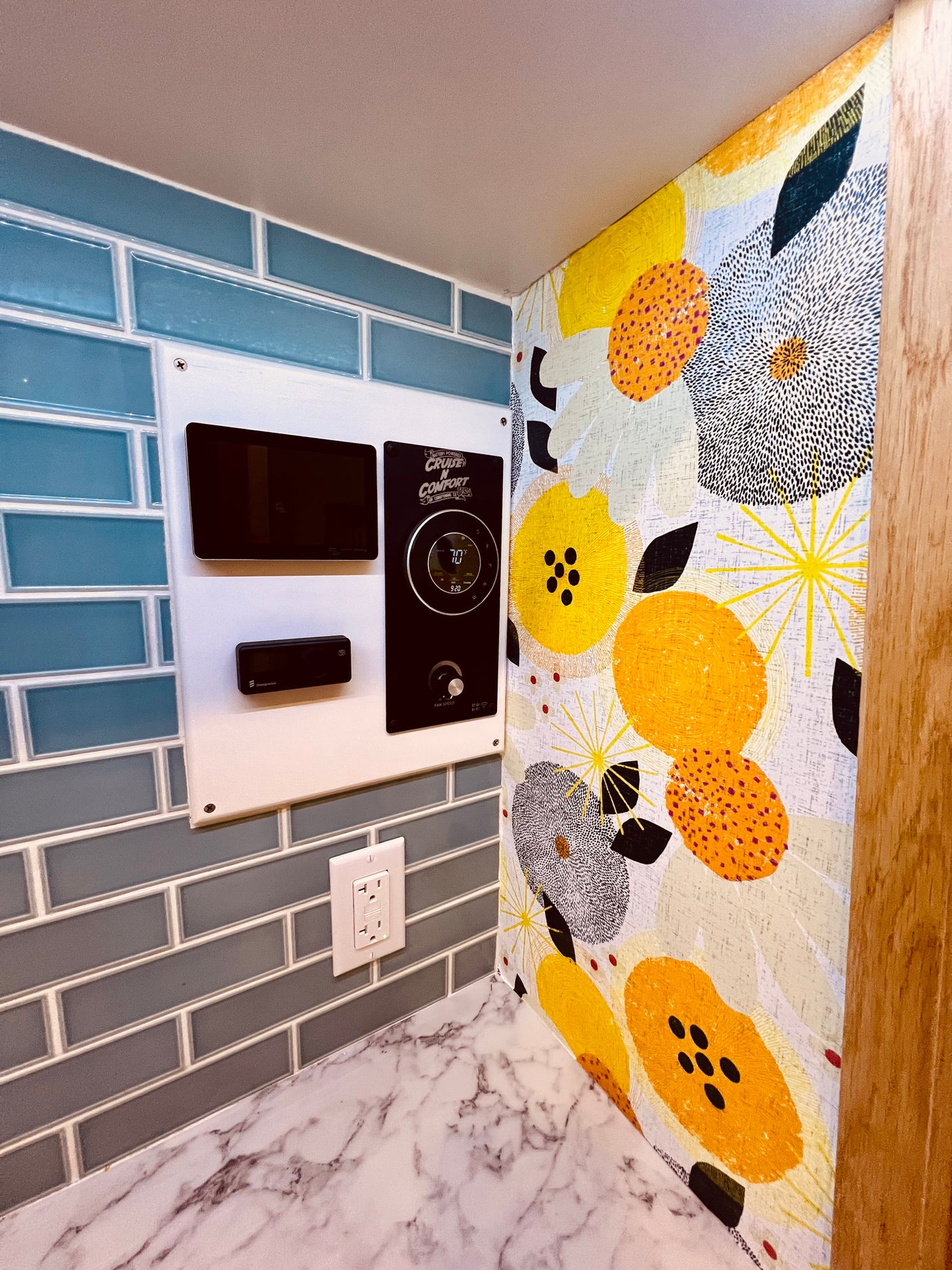 RV rental interior showcasing a comfort control panel, blue tile, marble countertop, and bold floral wallpaper.