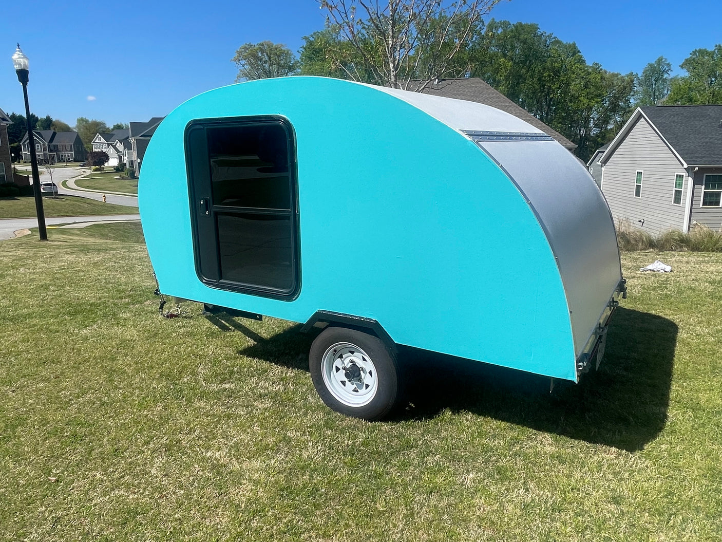 Vibrant turquoise teardrop RV rental, a compact travel trailer, sits on a bright green lawn.