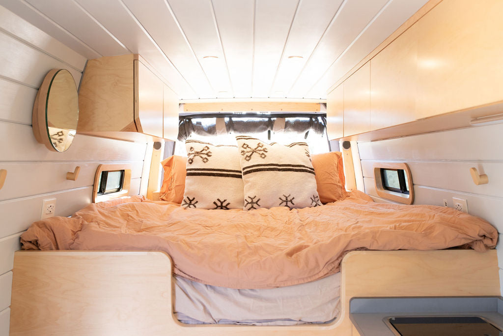 An inviting bed in a light wood-paneled RV rental, showing a cozy, well-designed van interior.