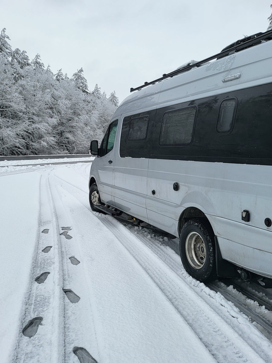 White RV rental on a snowy road with frosted trees and footprints visible in winter.