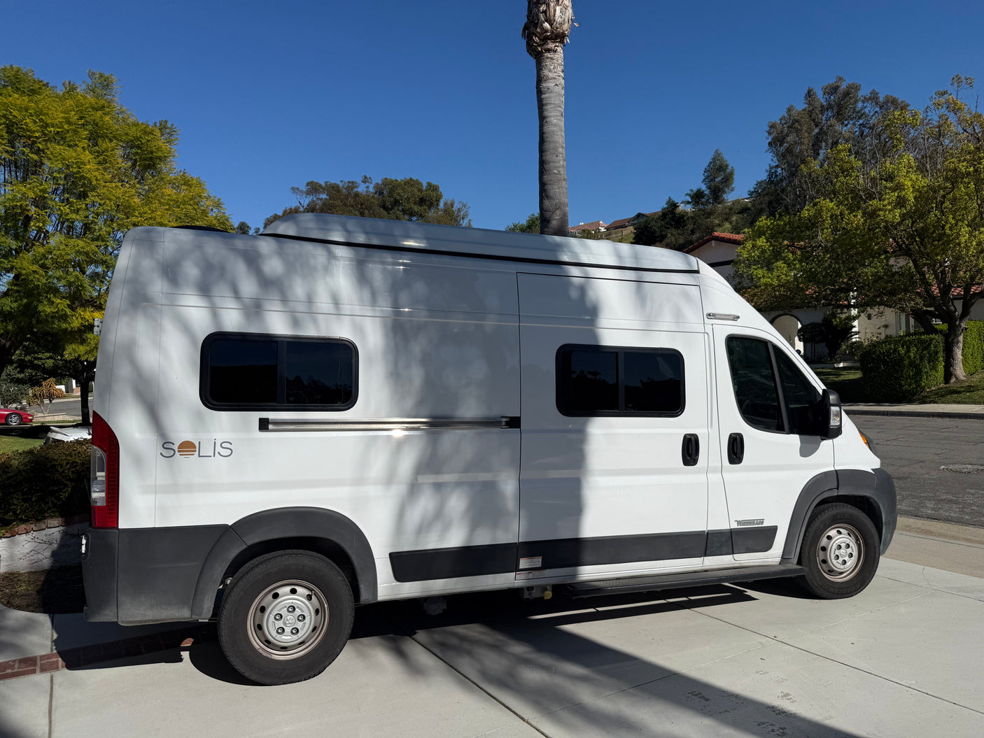 A white Winnebago Solis camper van, ideal for RV rental adventures, parked on a sunny concrete drive.