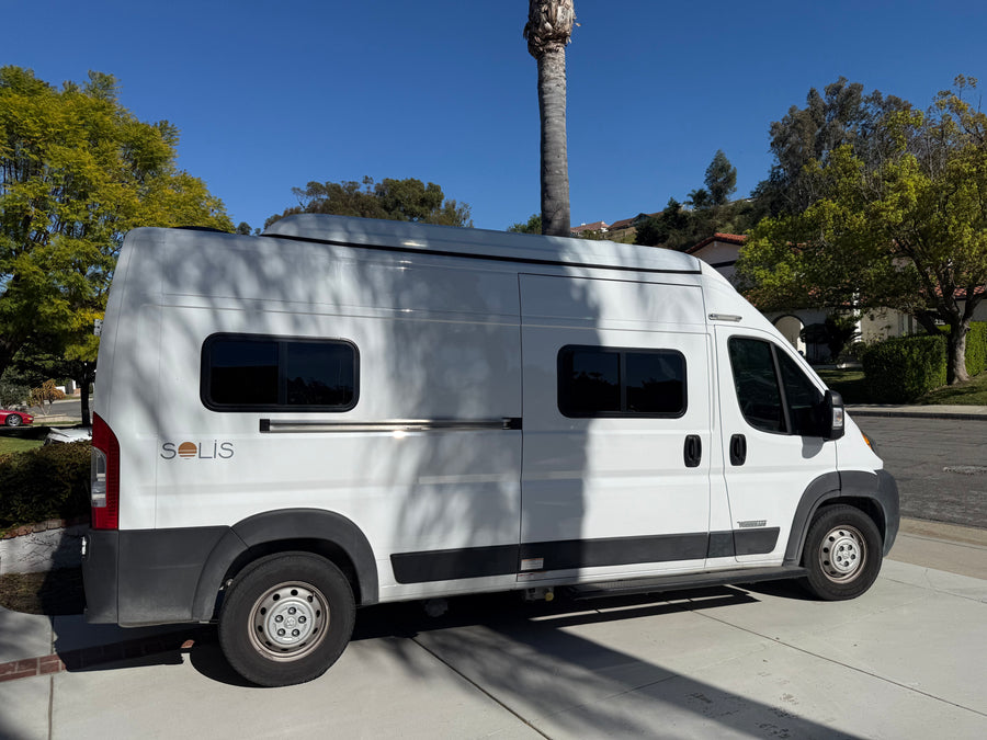 A white Winnebago Solis camper van, ideal for RV rental adventures, parked on a sunny concrete drive.