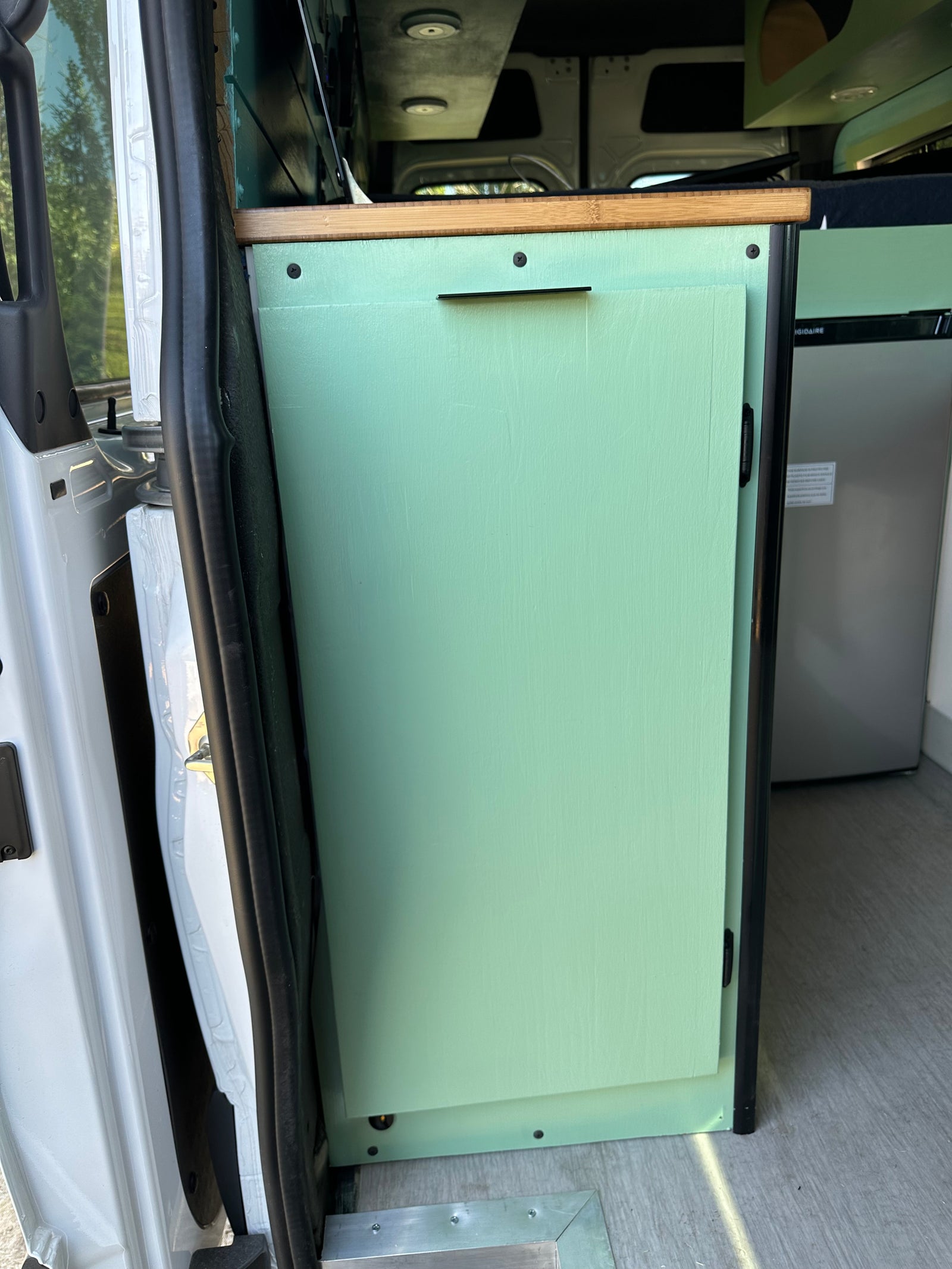 This RV rental interior features a mint green custom cabinet, wood countertop, and refrigerator, ideal for van life.