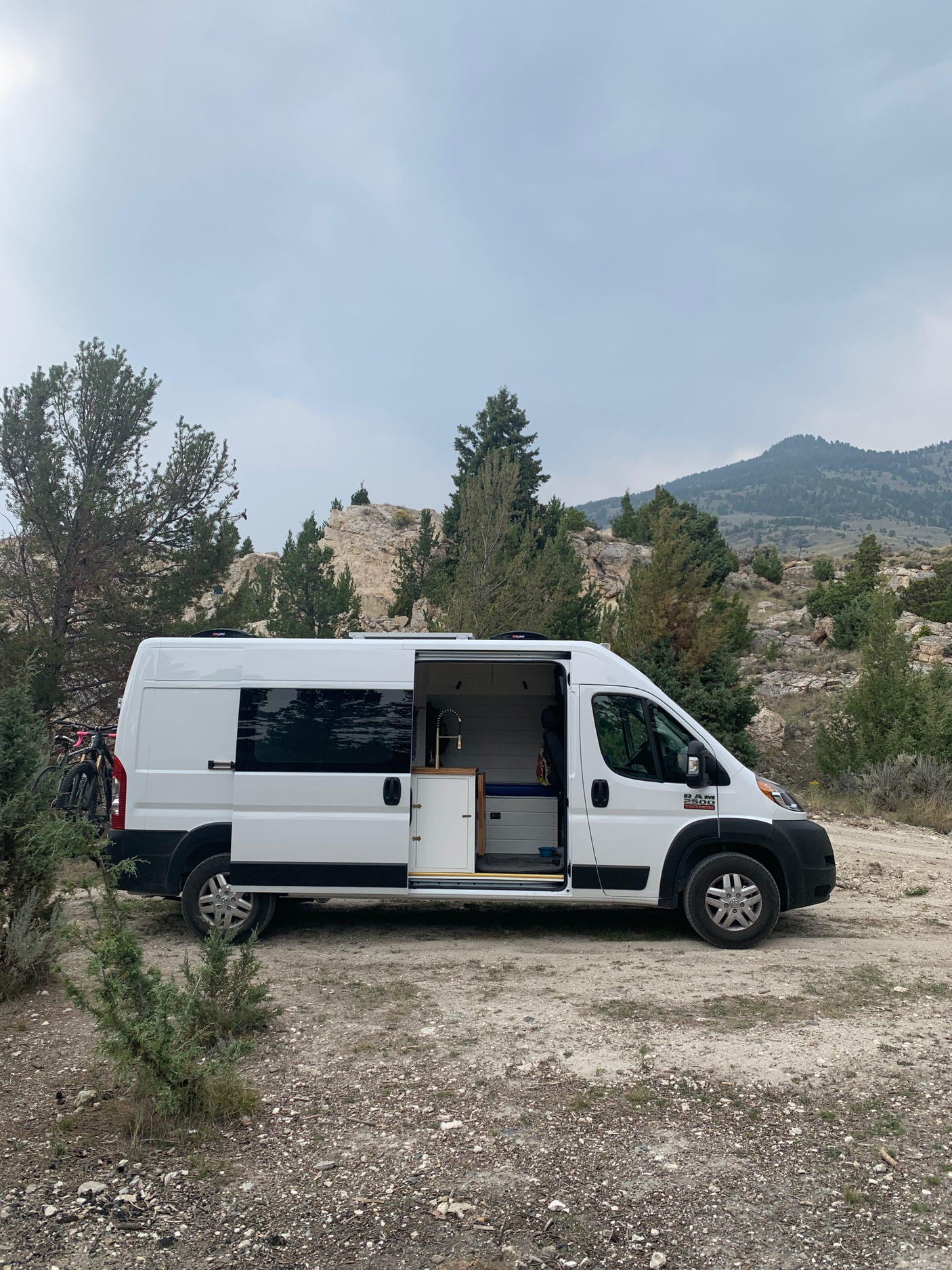 White camper van (RV rental) with open side door revealing interior, parked in a rocky mountain landscape. Perfect for van life.