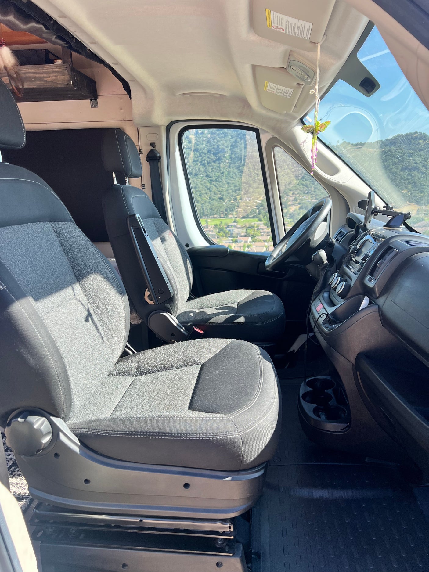 RV rental's front cabin with dark gray driver and passenger seats, dashboard, and a clear view of green hills outside.