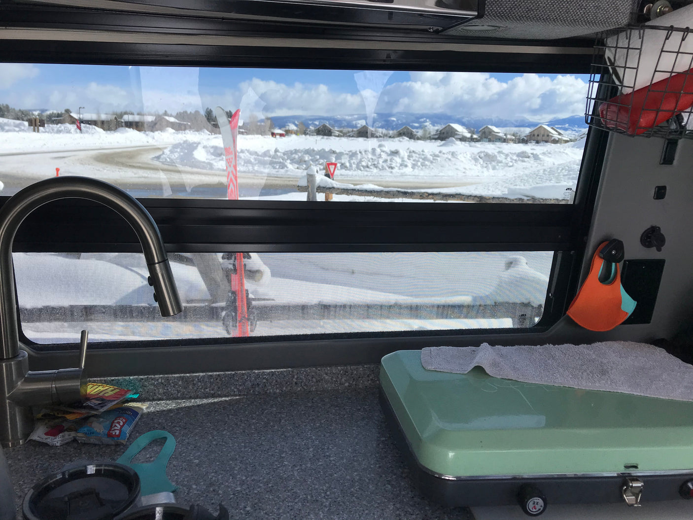 Cozy RV rental interior shows sink, stove, & a snowy vista with skis outside. Ideal for winter travel.