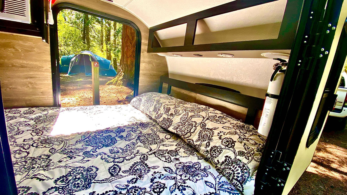 RV rental interior: a comfy bed overlooks a peaceful forest campsite with a blue tent. Ideal for glamping trips. — photo 8