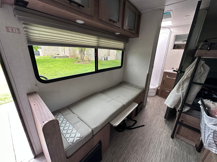 RV rental interior: Dinette converts to a bed, with a window, bathroom, and bunk beds visible in this compact living space.
